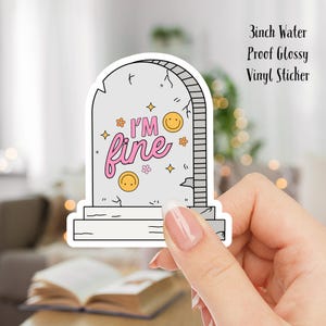 May include: A 3 inch water-proof glossy vinyl sticker featuring a tombstone with the text "I'm fine" in pink lettering and a smiling face. The tombstone is decorated with small flowers and stars.