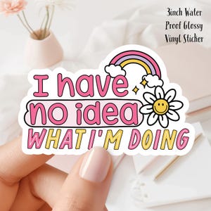 以下が含まれることがあります： ピンクと黄色の文字で「I have no idea what I'm doing」と書かれたカラフルなビニールステッカー。虹、笑顔のデイジー、そして「3inch Water Proof Glossy Vinyl Sticker」の文字が特徴です。