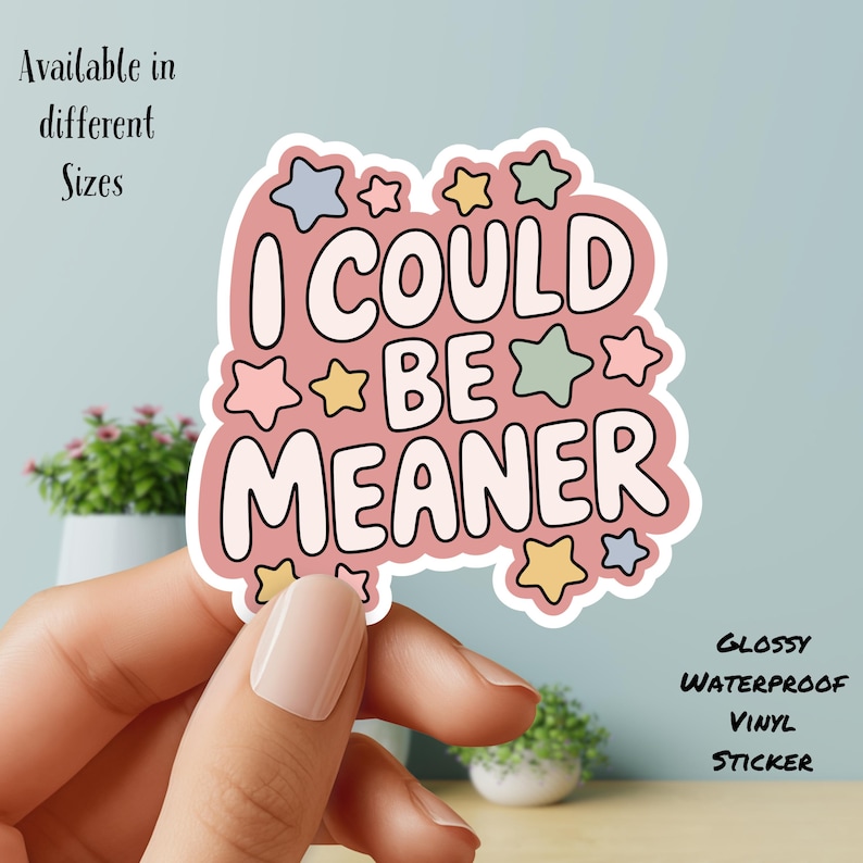 May include: A pink sticker with the text "I COULD BE MEANER" in a playful font, surrounded by colorful star shapes. The sticker is glossy and waterproof, with additional text indicating it's available in different sizes.