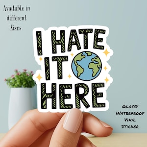 May include: Glossy waterproof vinyl sticker with the text "I HATE IT HERE" in black, with a blue and green Earth graphic. The sticker is available in different sizes.
