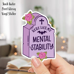 May include: A 3 inch water-proof glossy vinyl sticker featuring a purple tombstone with a white cross, a bat, and the text "Here Lies My Mental Stability". The tombstone is decorated with pink roses.