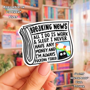 May include: A white sticker with the headline "BREAKING NEWS" and the text "ALL I DO IS WORK & SLEEP. I NEVER HAVE ANY MONEY AND I'M ALWAYS FUCKING TIRED." A small image of a black cat under a rainbow is included.