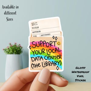 Puede incluir: Una pegatina de vinilo brillante que muestra un sobre de tarjeta de biblioteca con un gráfico de arcoíris y el texto SUPPORT YOUR LOCAL DATA CENTER (THE LIBRARY) en negro, con un pequeño smiley amarillo y diamantes.