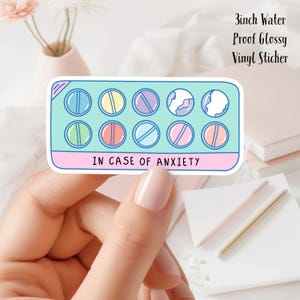 May include: A 3-inch water-proof, glossy vinyl sticker featuring a pill pack design with colorful pills. The sticker has the text "IN CASE OF ANXIETY" at the bottom. The pills are in shades of blue, yellow, purple, pink, and green.