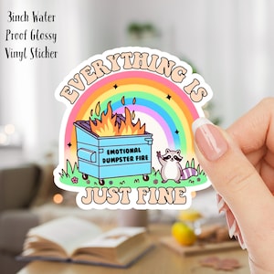 Pode incluir: Um adesivo de vinil brilhante à prova d'água de 7,6 cm com um arco-íris, um incêndio em um contêiner de lixo e um guaxinim. O texto no adesivo diz "Everything is Just Fine" e "Emotional Dumpster Fire".