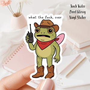 May include: A vinyl sticker featuring a cartoon frog wearing a cowboy hat, red bandana, and cowboy boots, holding a walkie-talkie. The sticker has the text "what the fuck, over" and is 3 inches in size.