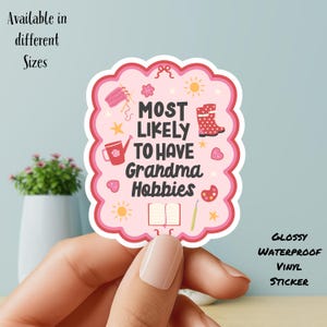 May include: A pink, glossy, waterproof vinyl sticker with a scalloped edge. The sticker reads "MOST LIKELY TO HAVE Grandma Hobbies" with illustrations of knitting, gardening, and painting. Text at the top says "Available in different Sizes".