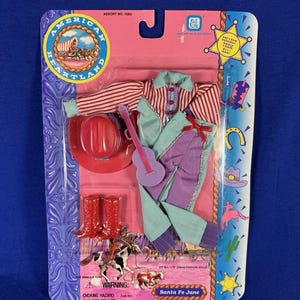 May include: A Santa Fe Jane doll outfit, packaged on a pink and purple card. The set includes a red cowboy hat, red boots, a striped shirt, a turquoise top, purple pants, and a small purple guitar. The package reads "American Heartland."
