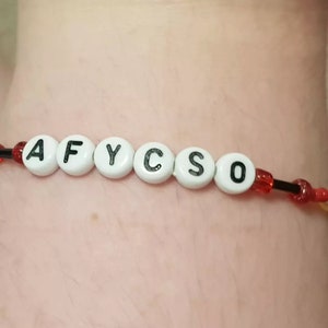 May include: A beaded bracelet with white letter beads spelling out "AFYCSO". The bracelet features red and black beads strung on a black cord. The bracelet is shown on a person's wrist.