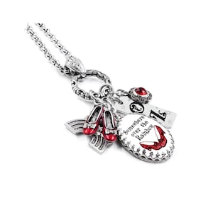 May include: Silver-toned necklace with multiple charms. Charms include a pair of red shoes, a rainbow, a tag with the letter "Z", and an oval charm with the text "Somewhere over the Rainbow" and a red shoe illustration.