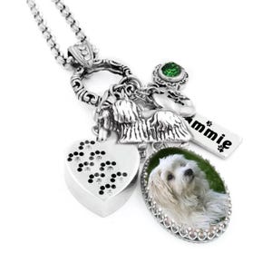A silver necklace with various charms and a heart-shaped charm featuring a photo of a white dog.