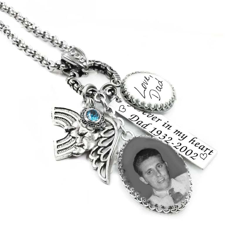 A silver-toned necklace with various charms and pendants, including a charm with a photo of a man and a charm with the words "Love Dad" written on it.
