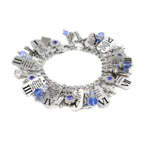 May include: A silver-tone charm bracelet featuring ten rectangular metal tags engraved with Roman numerals I through X and corresponding biblical commandments. The bracelet includes blue crystal beads, small cross charms, and angel figures.