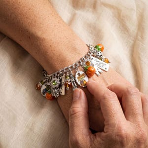 May include: A silver-tone charm bracelet featuring various autumn-themed pendants including orange pumpkins, green and amber beads, a scarecrow, and a rectangular tag engraved with the text Pumpkin Patch and another with Fall Harvest.