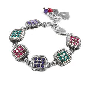 May include: A silver-toned chain bracelet featuring five square links, each embedded with small purple, red, or green crystals. The bracelet includes a lobster claw clasp and three dangling charms: a purple crystal, a red crystal, and a heart-shaped tag.