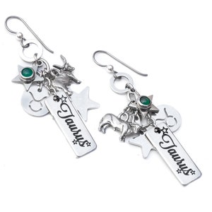 May include: Silver-toned dangle earrings featuring charms related to the Taurus zodiac sign. Each earring has a hook, a ring, a green gemstone, a star, a Taurus symbol, a goat, a bull, and a rectangular charm with the word "Taurus".