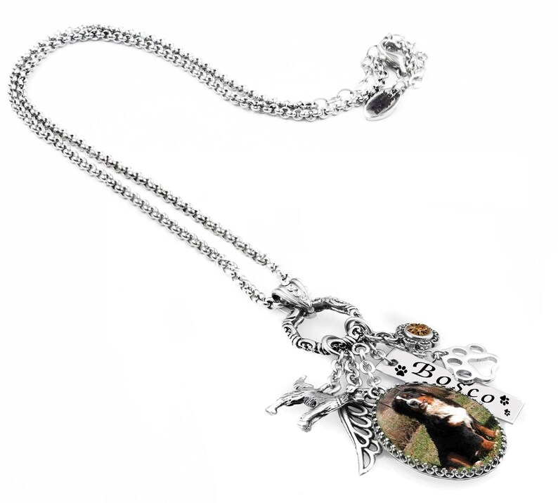 a silver necklace with various charms and pendants, including a charm that says "Bosco" and a charm depicting a dog.