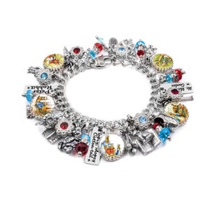 May include: A silver-tone charm bracelet featuring multiple Peter Rabbit themed charms, including circular illustrations of rabbits, red and blue crystal beads, and rectangular metal tags with text reading Peter Rabbit and Flopsy Mopsy Cotton-tail.