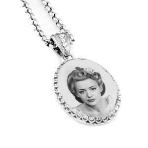 May include: A silver-toned oval pendant necklace featuring a black and white portrait of a person with vintage-style hair. The pendant is framed by a beaded edge and suspended from a matching silver chain with small clear crystals on the bail.