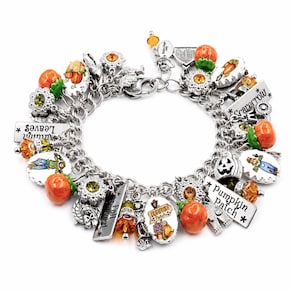 May include: A silver-tone charm bracelet featuring various autumn-themed charms including orange pumpkins, scarecrows, and rectangular metal tags with the text Autumn Leaves, Scarecrow, and Pumpkin Patch, accented with orange and green crystals.
