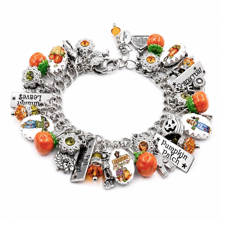 May include: A silver-tone charm bracelet featuring various autumn-themed charms including orange pumpkins, scarecrows, and rectangular metal tags with the text Autumn Leaves, Scarecrow, and Pumpkin Patch, accented with orange and green crystals.