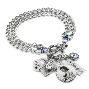 May include: Silver charm bracelet with multiple charms. Charms include a camera, a heart with the name "Kari", a tag that says "I Photography", and a circular charm with a black and white photo.