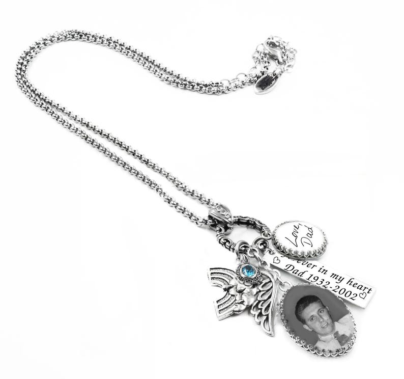 a silver necklace with various charms and a pendant, including a small picture of a man and some text.