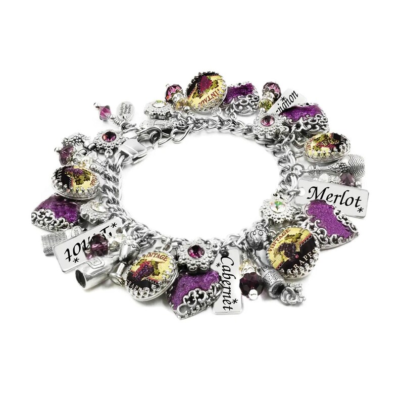 A silver charm bracelet with purple and white charms featuring wine-themed designs, including grapes, wine bottles, and the words "Merlot", "Cabernet", and "Vintage".