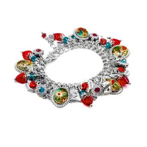 May include: A silver-tone charm bracelet featuring multiple round pendants with colorful illustrations of cherubs and hearts, interspersed with red and blue faceted beads, small silver heart charms, and rectangular tags labeled FRAGILE.
