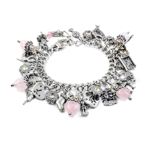 May include: A silver-toned charm bracelet featuring a variety of dangling ornaments, including heart-shaped charms with engraved letters, small pink translucent beads, metallic figures, and floral-shaped charms with embedded iridescent crystals.