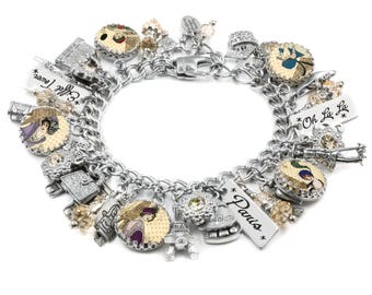 May include: A silver-tone charm bracelet featuring multiple dangling charms including circular portraits of people in vintage attire, a miniature Eiffel Tower, and rectangular metal tags inscribed with the words Paris, Oh La La, and Eiffel Tower.