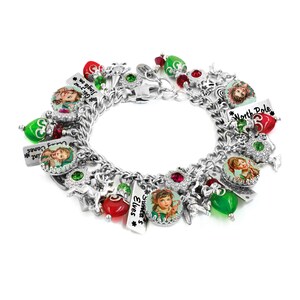 May include: A silver charm bracelet featuring multiple holiday-themed charms, including round portraits of elves, red and green faceted beads, and rectangular metal tags with text reading North Pole, Santa's Elves, and Get your Jingle on.