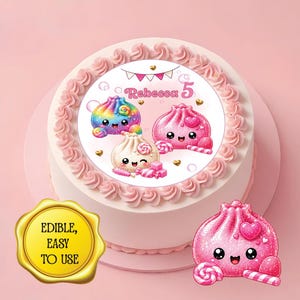 May include: A round cake topped with a circular edible image featuring three kawaii-style dumplings, pink hearts, and the text "Rebecca 5". The cake has pink frosting swirls along the edge. A separate pink dumpling cutout and a gold seal are included.