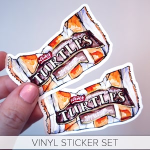 May include: A set of two vinyl stickers featuring a watercolor illustration of a Nestle Turtles chocolate bar. The stickers are white with a brown, orange, and white design.
