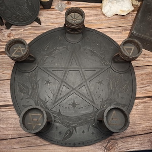 May include: A dark grey wooden altar featuring a pentagram design, with five small candle holders. The altar has etched botanical and celestial details. The candle holders have geometric symbols. The overall theme is Wiccan and spiritual.
