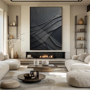 May include: A modern living room interior with a black and white abstract painting hanging above a fireplace. The room is decorated in a minimalist style with beige furniture and a wooden coffee table.