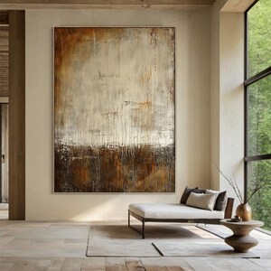 以下が含まれることがあります： 茶色、白、金色のトーンの抽象画。絵画はテクスチャのある表面と、上部と下部を分ける水平線を持っています。上部は主に白で、茶色と金色のアクセントがあります。下部は主に茶色で、金色のアクセントがあります。