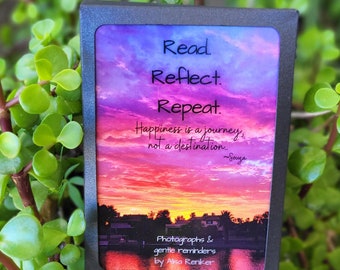 以下が含まれることがあります： 夕焼けの背景に「Read. Reflect. Repeat. Happiness is a journey, not a destination. ~Souza」と「Photographs & gentle reminders by Alisa Renker」のテキストが書かれた黒い額縁のカード。