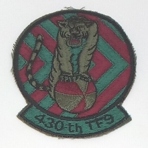 May include: Embroidered patch featuring a tiger perched atop a red and green striped ball. The tiger is olive green with a snarling expression. The patch has a green border and the text "430th TF9" at the bottom.