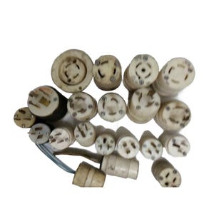 May include: A collection of various off-white electrical plugs and receptacles of different sizes and configurations. These cylindrical components feature metallic prongs and slots for power connections, with some units attached to short electrical wires.