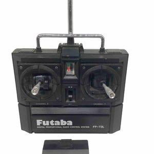 May include: A black Futaba FP-T2L digital proportional radio control system with a silver antenna and a black base. The control system has two channels, one on each side, with a switch for on and off.