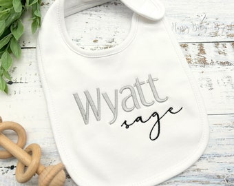 May include: White cotton baby bib with the name "Wyatt Sage" embroidered in gray and black thread.