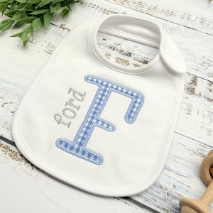 May include: White baby bib with a blue and white gingham letter F and the name Ford embroidered in silver thread.