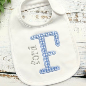 May include: White baby bib with a blue and white gingham letter E and the name Ford embroidered in gray.