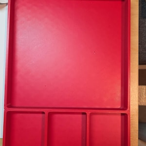 May include: A bright red plastic tray with a rectangular main compartment and three smaller square compartments. The tray has a textured surface and is designed for organizing small items.