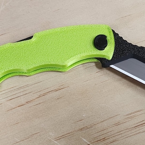 May include: A lime green folding knife with a black blade and handle accents. The knife has a textured grip and a ring at the base of the handle. The blade is silver and has a partially serrated edge.