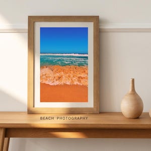 Puede incluir: Una fotografía enmarcada de una escena de playa con cielo azul, agua turquesa y arena naranja. Las olas rompen en la orilla, creando un borde blanco espumoso. El texto "BEACH PHOTOGRAPHY" está impreso debajo de la imagen.
