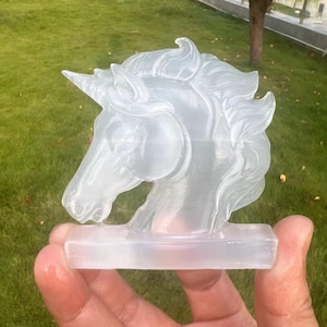 May include: A clear glass unicorn head sculpture with a detailed mane and horn. The sculpture is on a small, clear glass base.