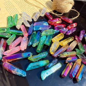 May include: A collection of iridescent crystal points in various colours, including pink, green, blue, yellow, and purple. The crystals are arranged on a black surface.