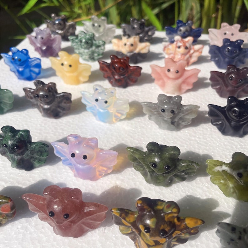 May include: A collection of small, carved bat figurines in various colors, including blue, pink, green, and brown. The bats have outstretched wings and detailed features, showcasing the craftsmanship of the stone carvings.